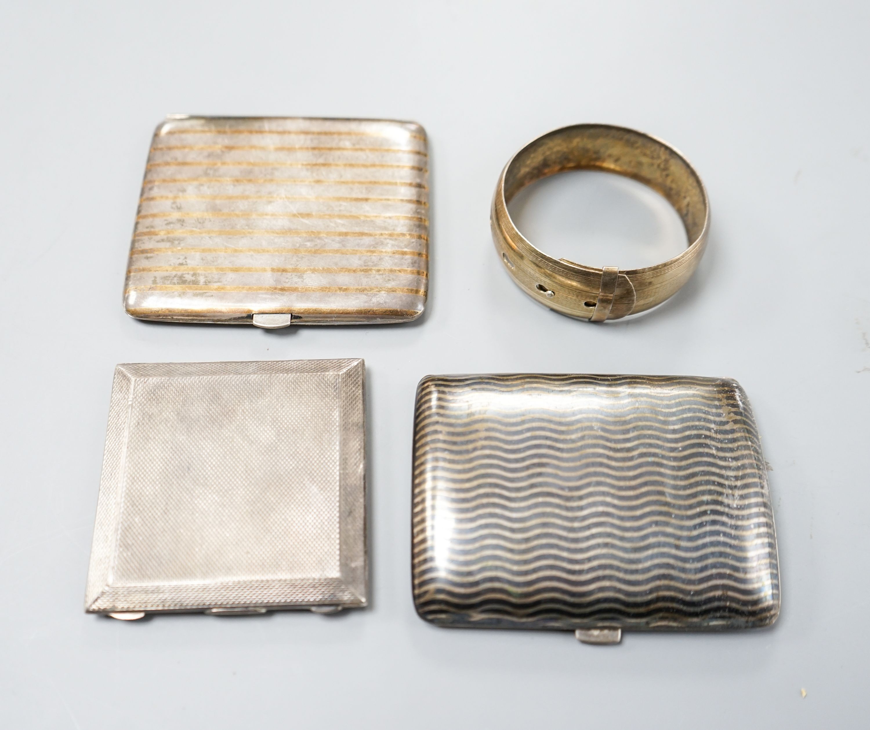 An 800 white metal and niello cigarette case,9cm, a Dutch gilt and white metal cigarette case, an engine-turned silver powder compact (a.f.) and a white metal bangle.